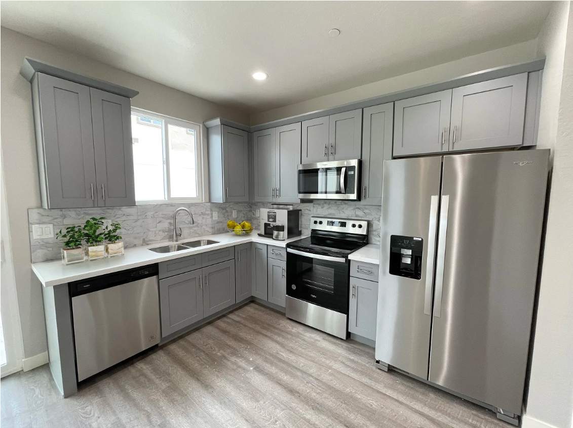 Modern kitchen with gray cabinets, stainless steel appliances, and light wood flooring