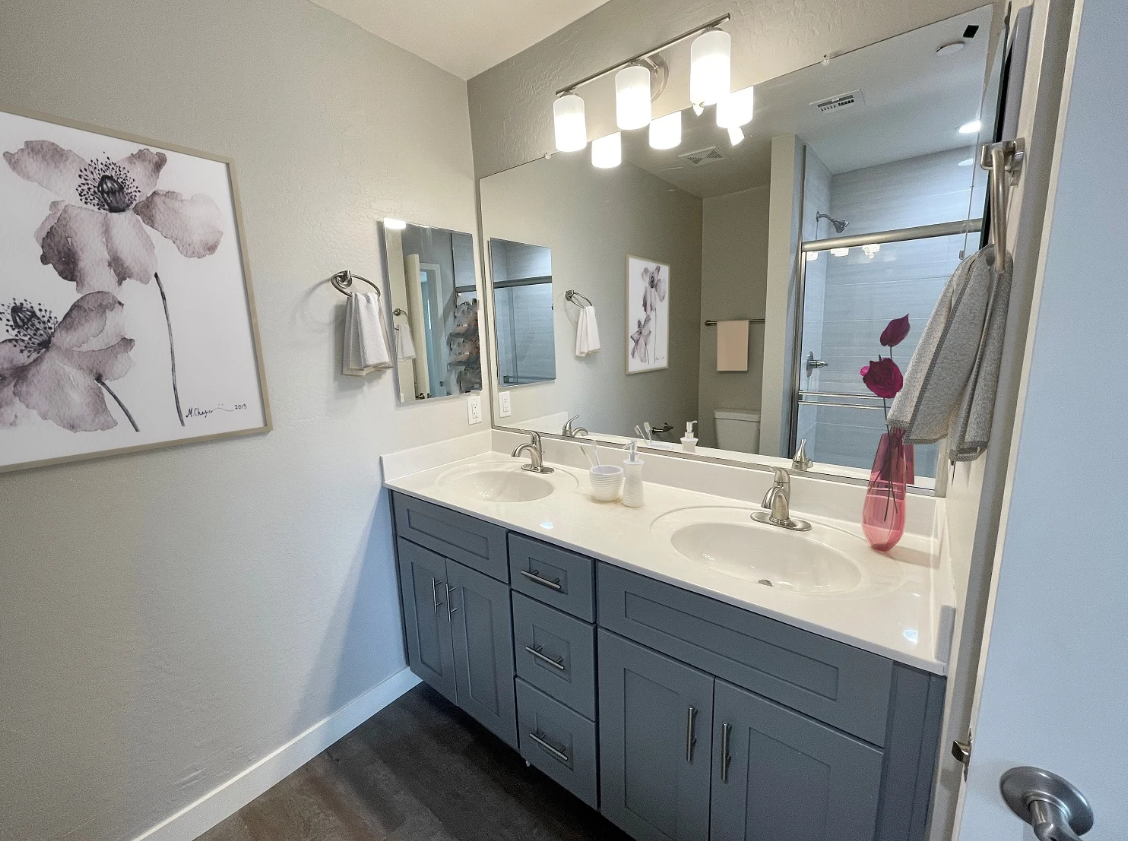 Modern bathroom vanity with blue cabinets, large mirror, and wall art.