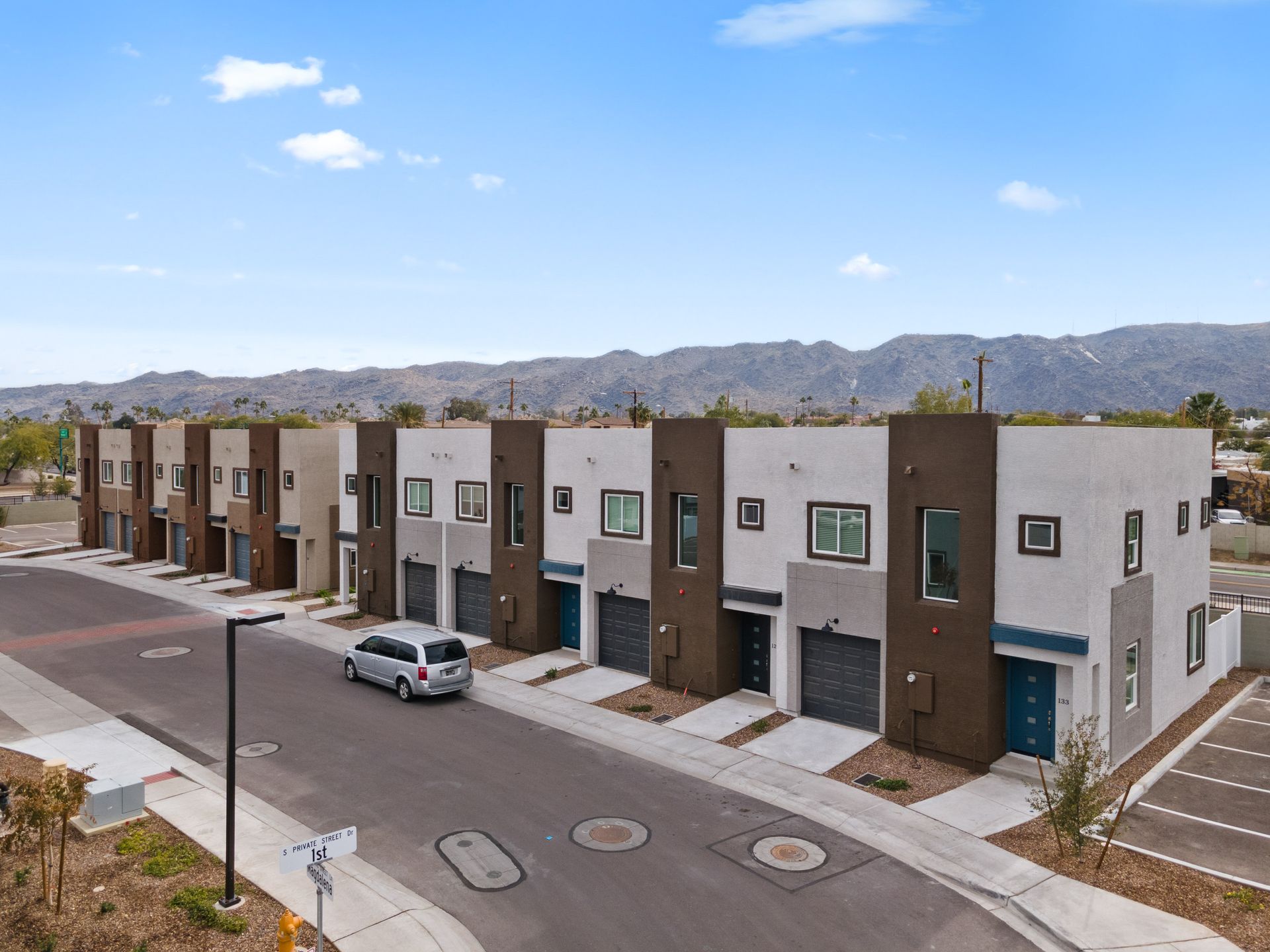 Modern row of townhouses with parked car on a quiet street, mountains in the background.