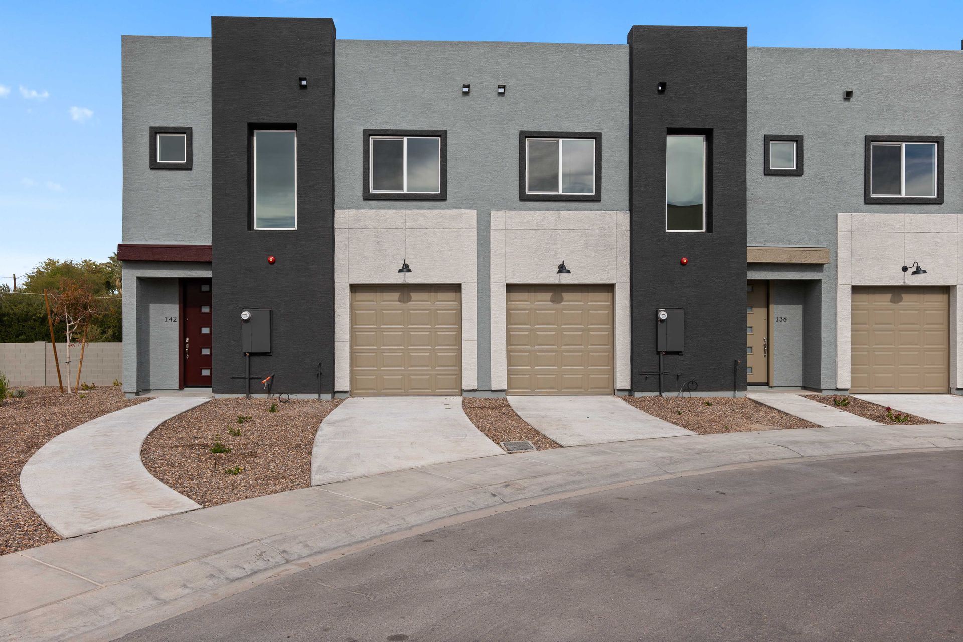 Row of modern townhouse units with garages and curved driveways under a cloudy sky