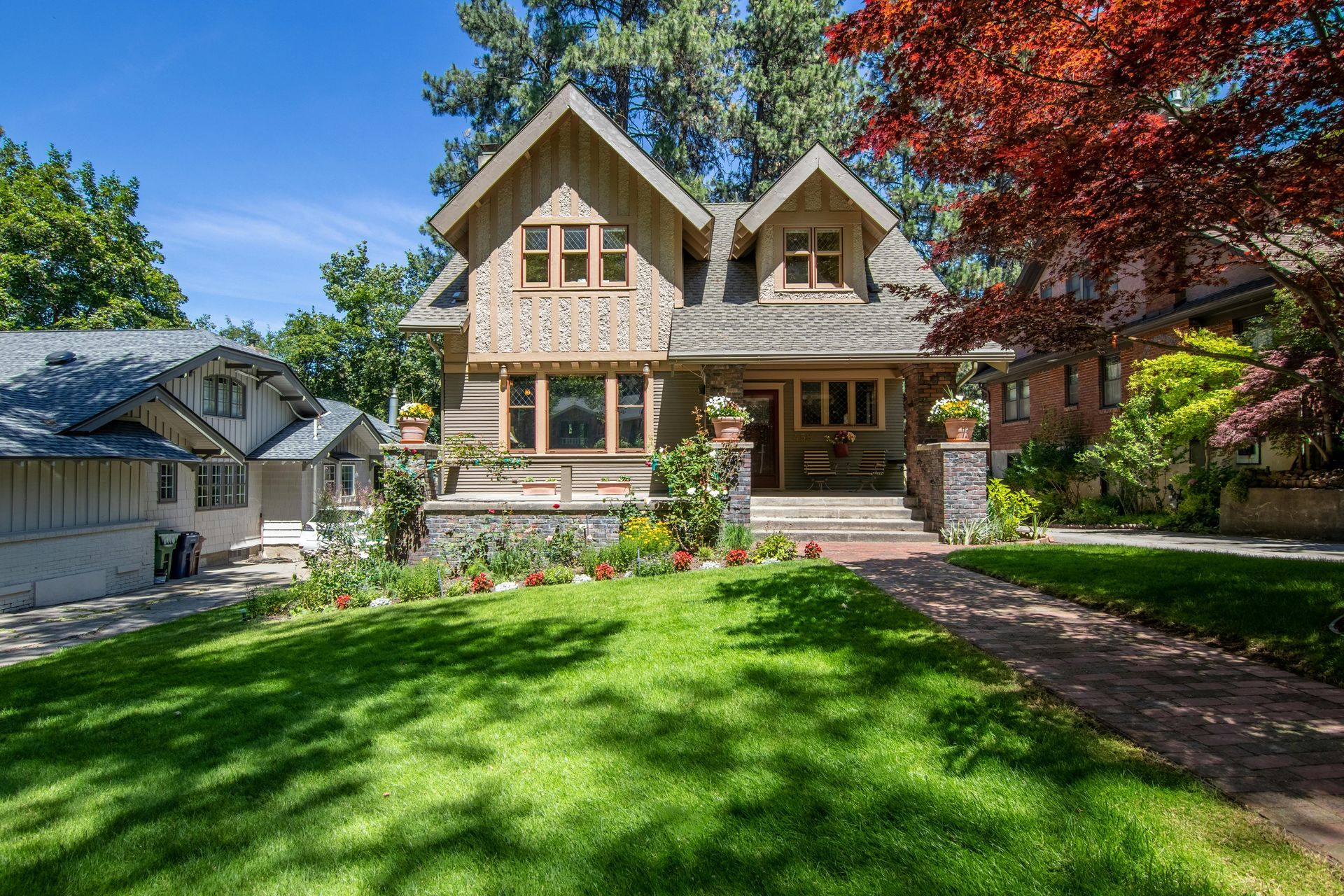 Two-story Craftsman home with a stone porch, gabled roof, and lush green lawn on a sunny day.