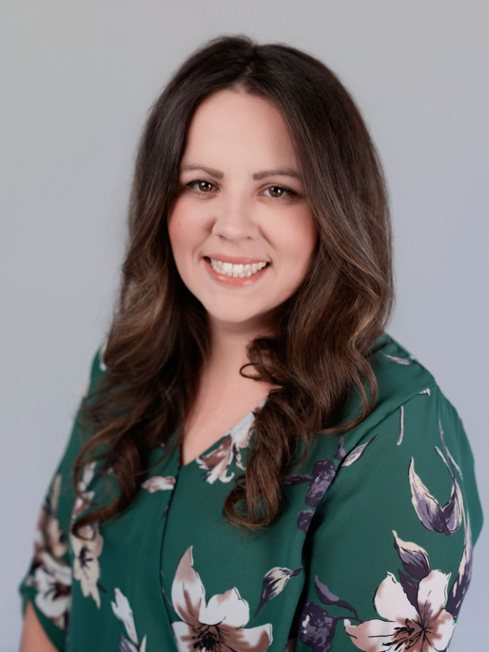 A woman in a blue dress and black jacket is smiling for the camera.