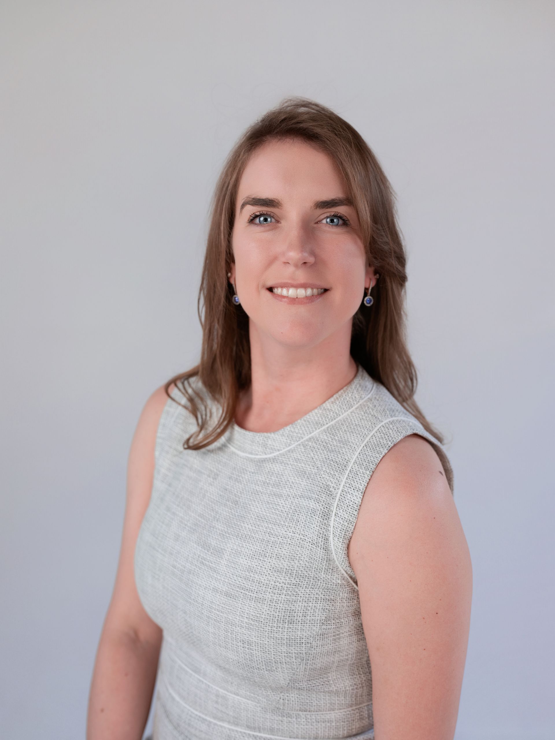 Woman with blonde hair wearing a white shirt and gray blazer smiles at the camera.