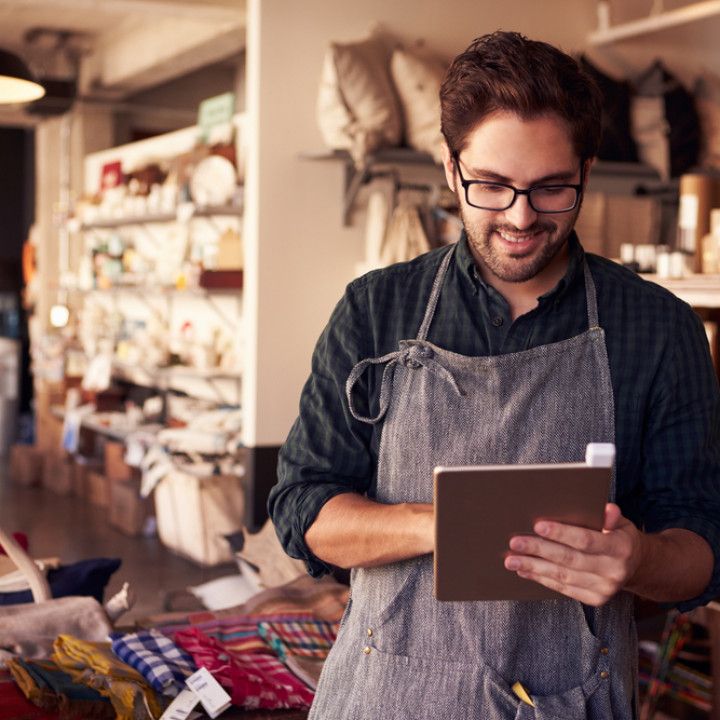 A man in an apron is using a tablet in a store.