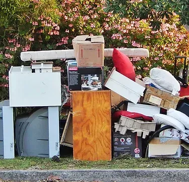 Pile of discarded items, including boxes, wood, and other household waste, set by a curb.