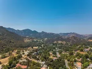 Aerial view of a valley with houses, trees, and mountains under a blue sky.
