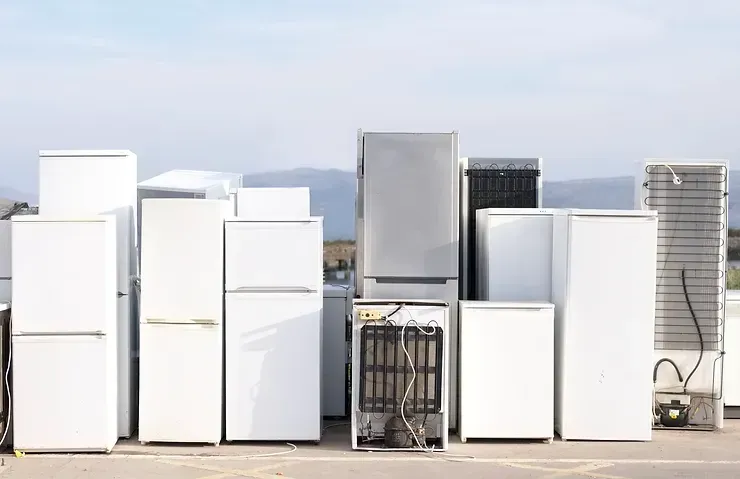 Assorted white refrigerators and freezers outdoors, lined up. Some show internal components.