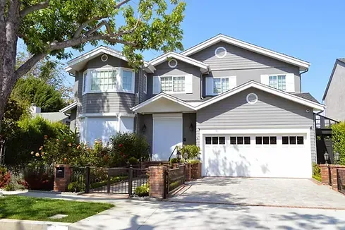 Gray two-story house with a white garage door, front yard, and brick and iron fence.