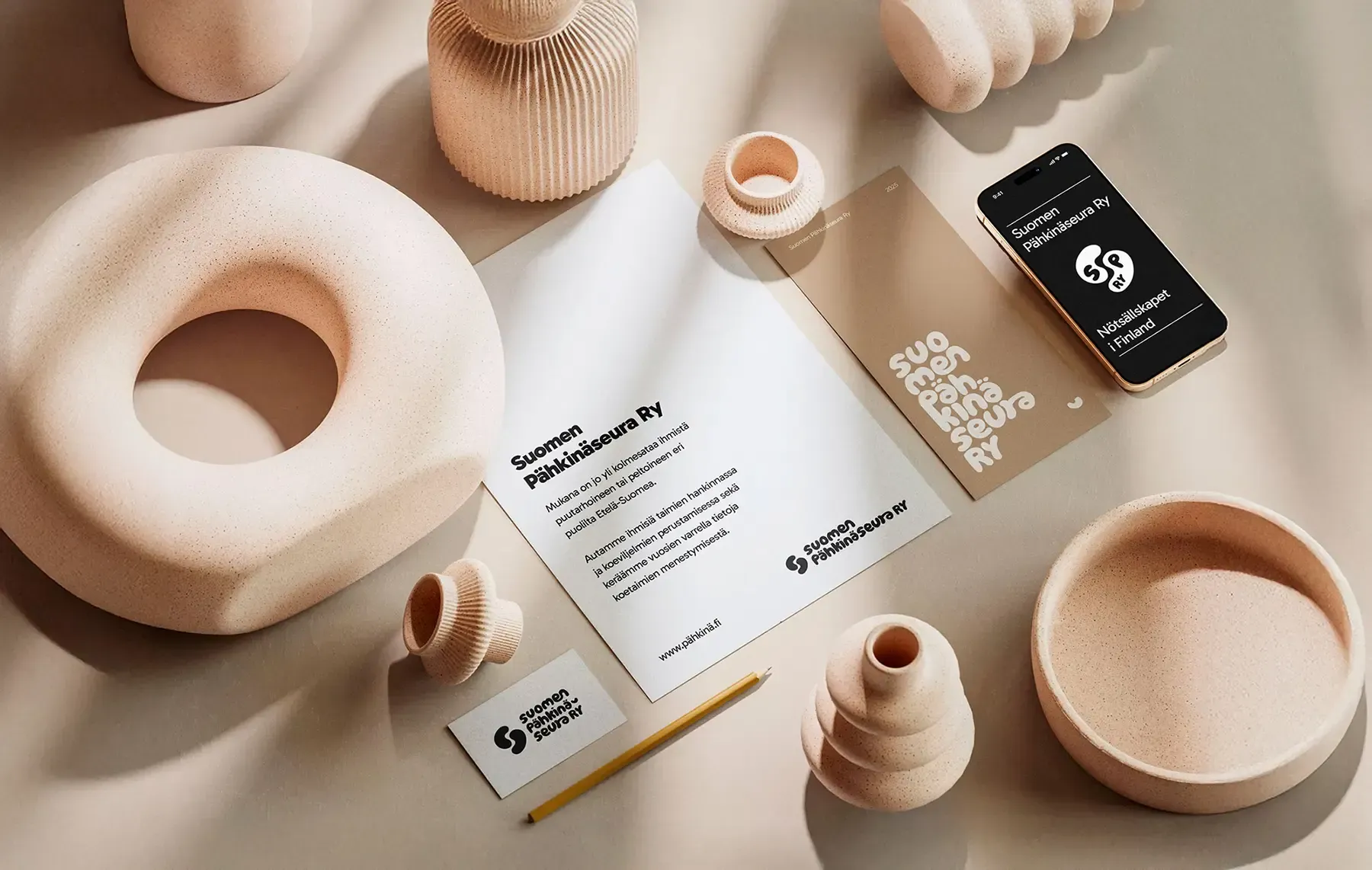 A stationery set, phone, and textured ceramic decor items in warm, neutral beige tones on a smooth surface.