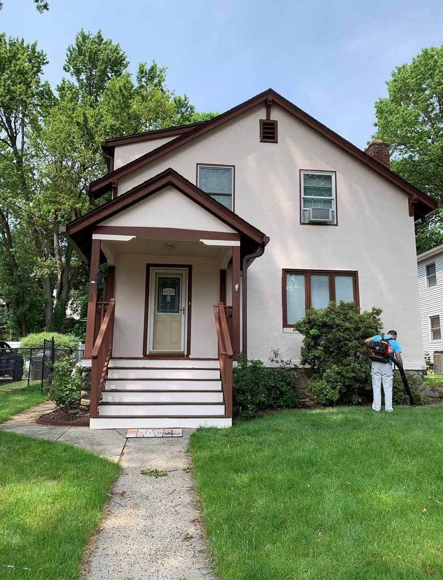 Two-story house with brown trim, front porch, and a person standing on the lawn.