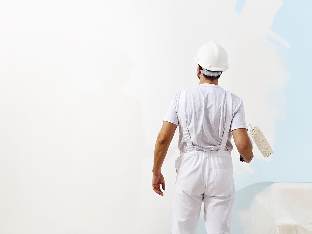 Worker in white coveralls and hard hat standing on a rooftop, holding a paint roller