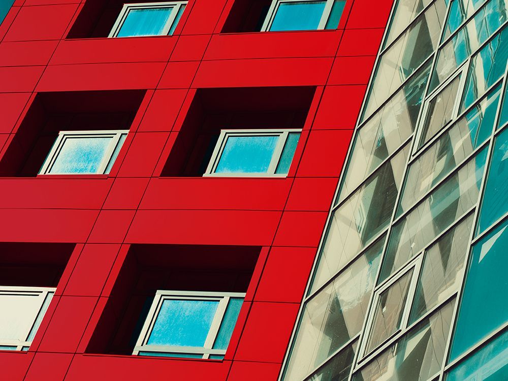 Red building facade with blue windows beside a glass-and-metal building