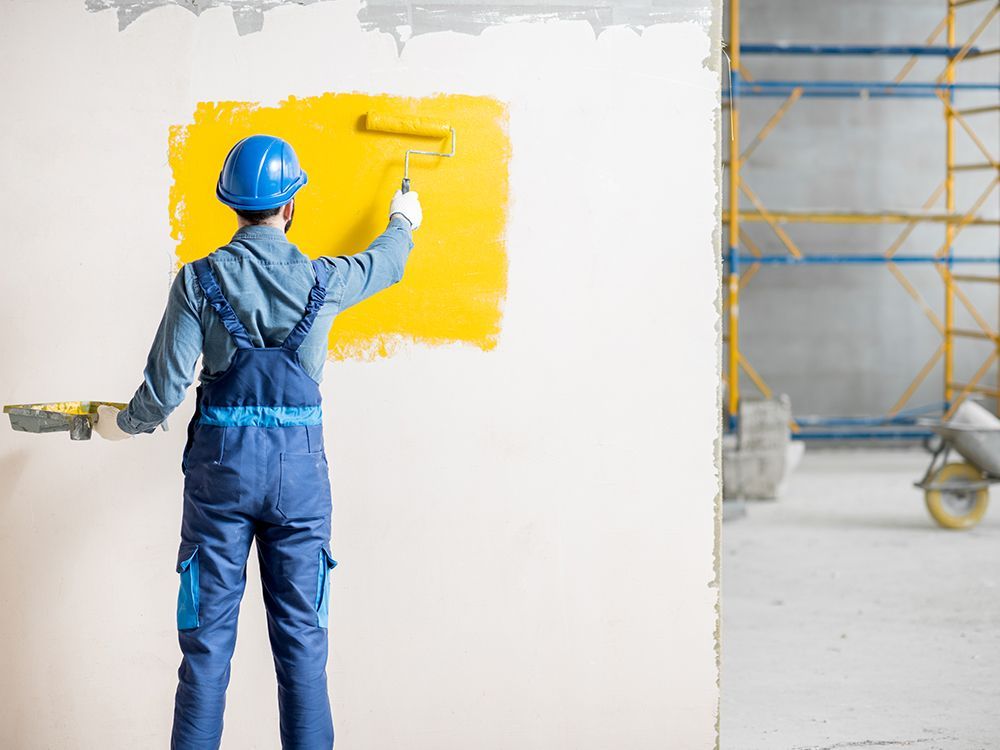 Worker painting a wall with bright yellow paint in a construction area
