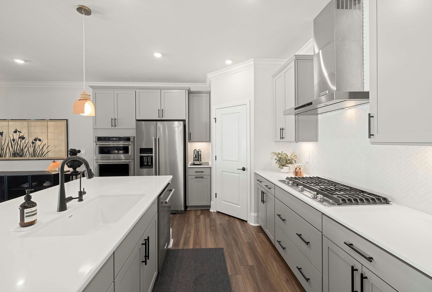 Bright modern kitchen with white cabinets, gray drawers, island, stainless steel appliances, and wood floors