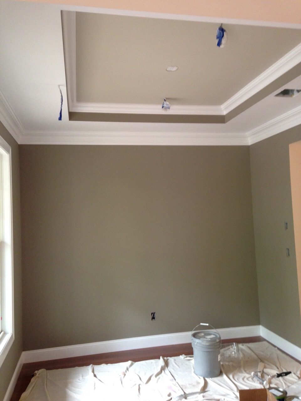 Empty room with gray walls, white trim, and a tray ceiling under renovation, with floor protection down.