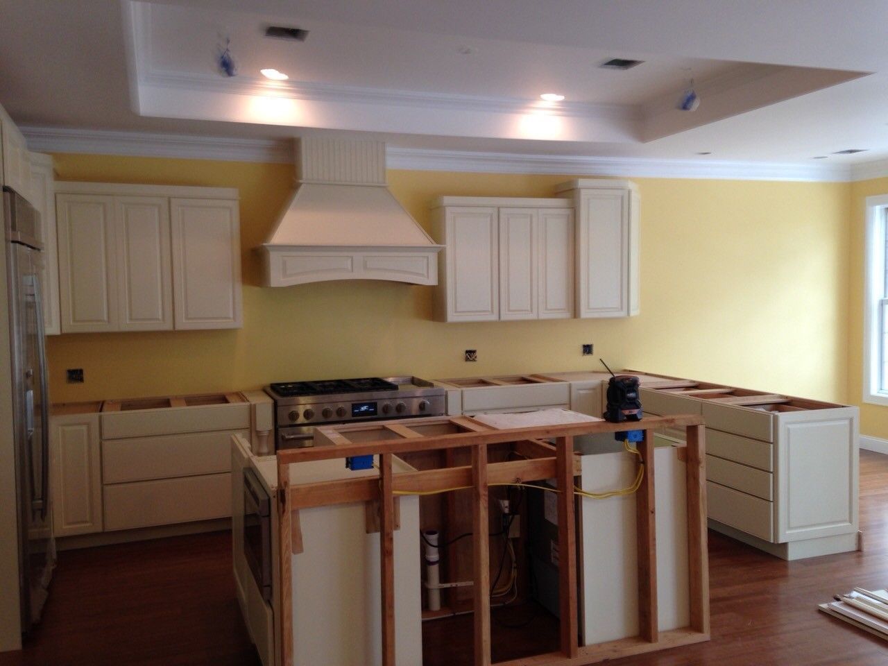 Empty kitchen with cream cabinets, yellow walls, and a central island under construction.