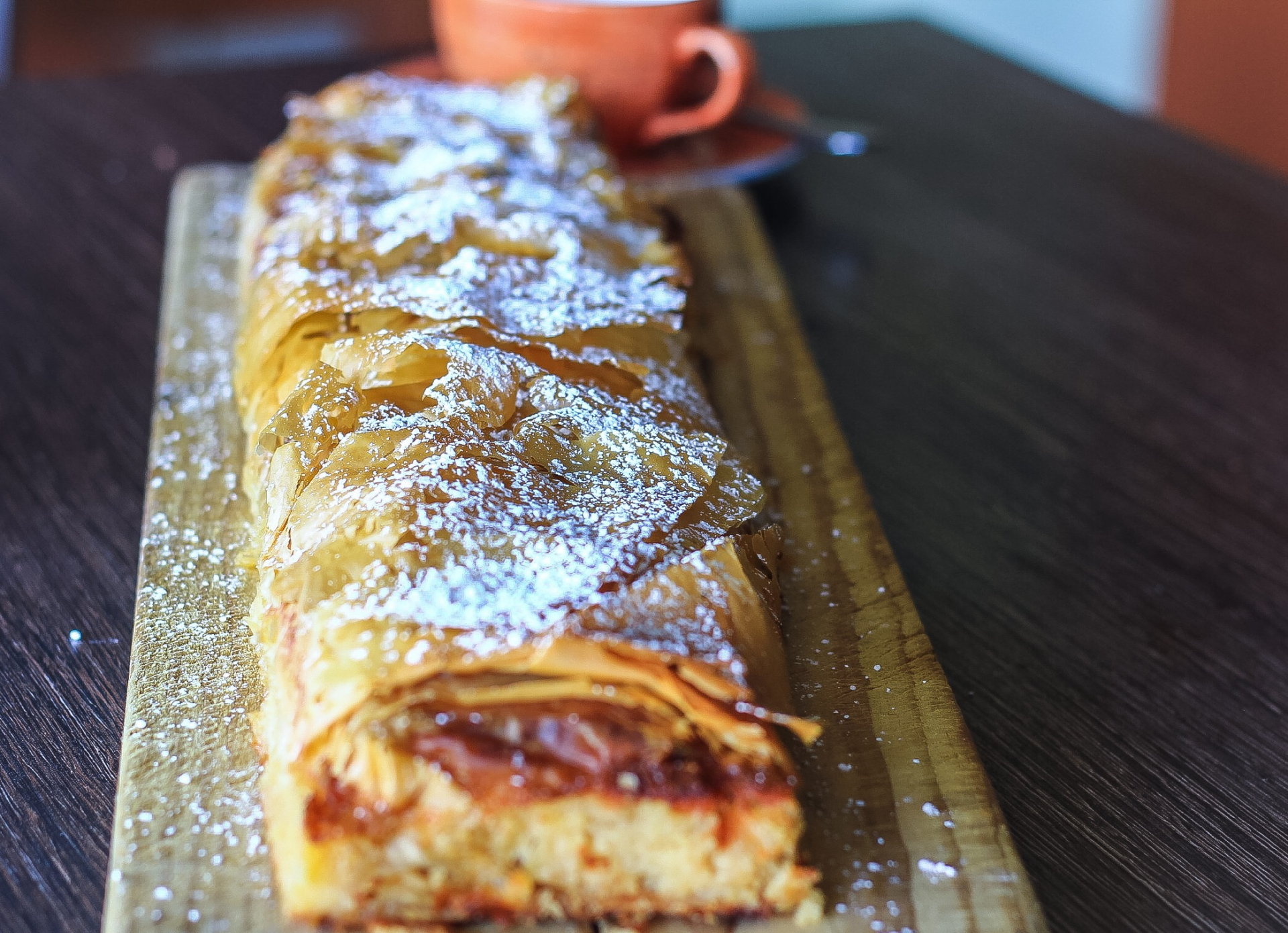 a pastry is sitting on a wooden cutting board next to a cup of coffee .