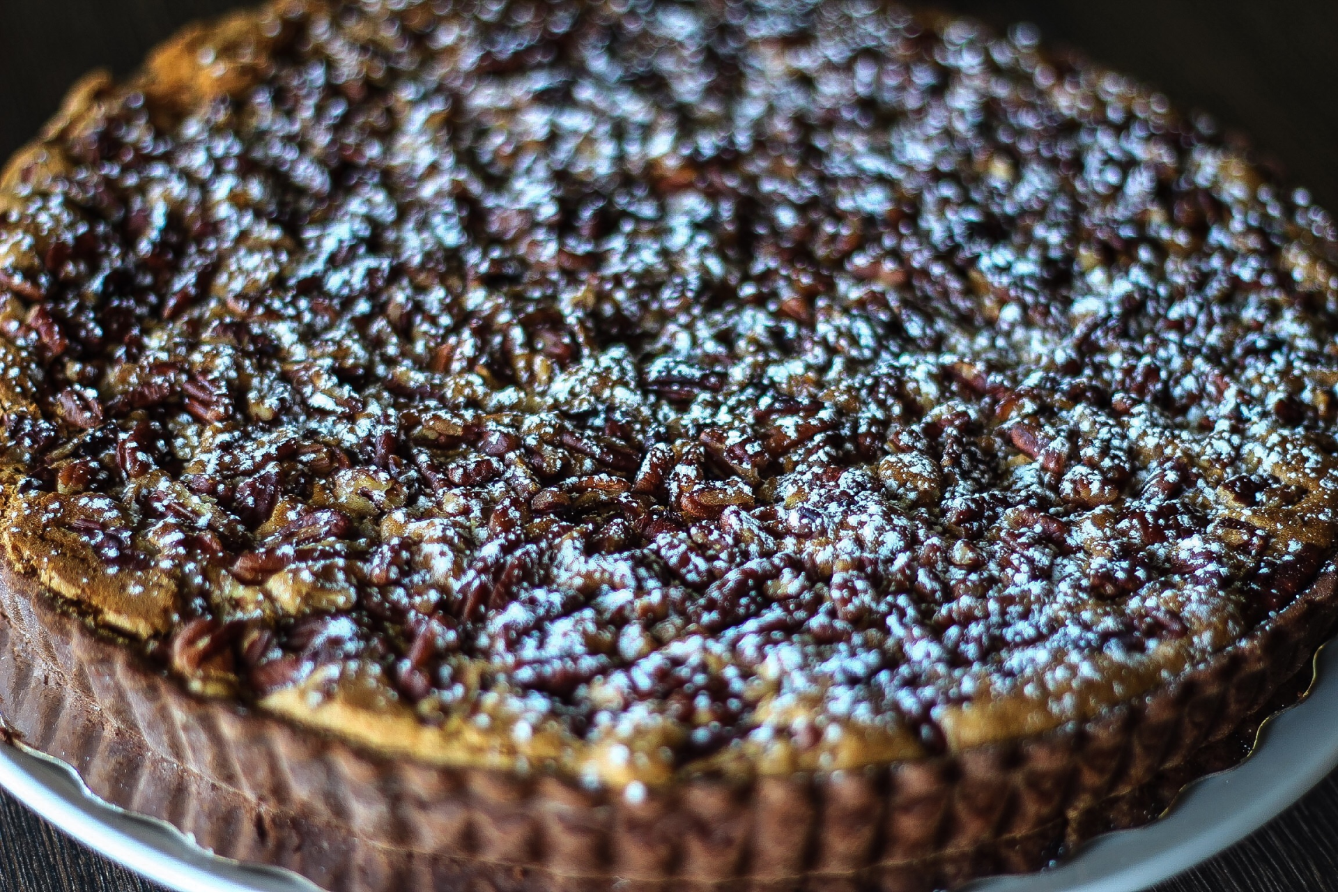 a pecan pie with powdered sugar on top is on a white plate .