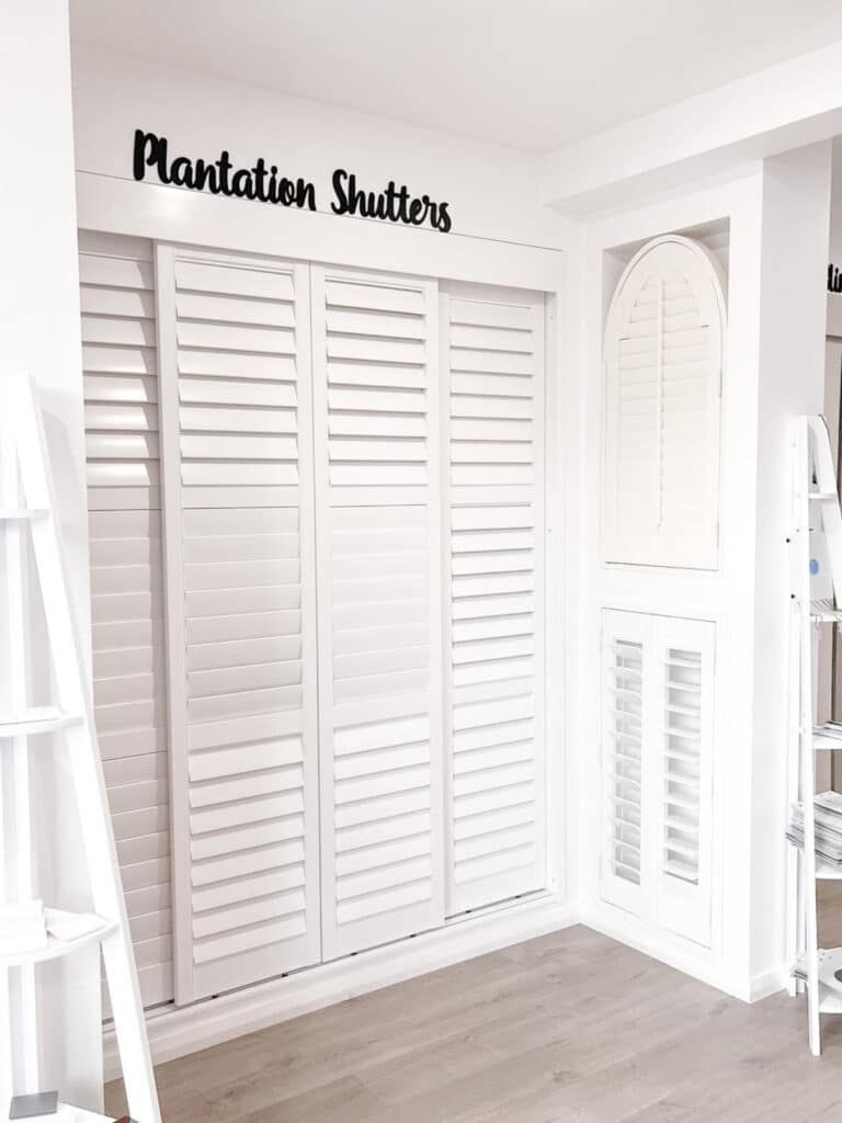 A Room with White Shutters on The Wall and A Sign that Says Plantation Shutters — Phoenix Blinds In Albion Park Rail, NSW