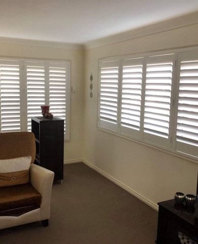 A Living Room with A Couch , Chair and Shutters on The Windows — Phoenix Blinds In Albion Park Rail, NSW
