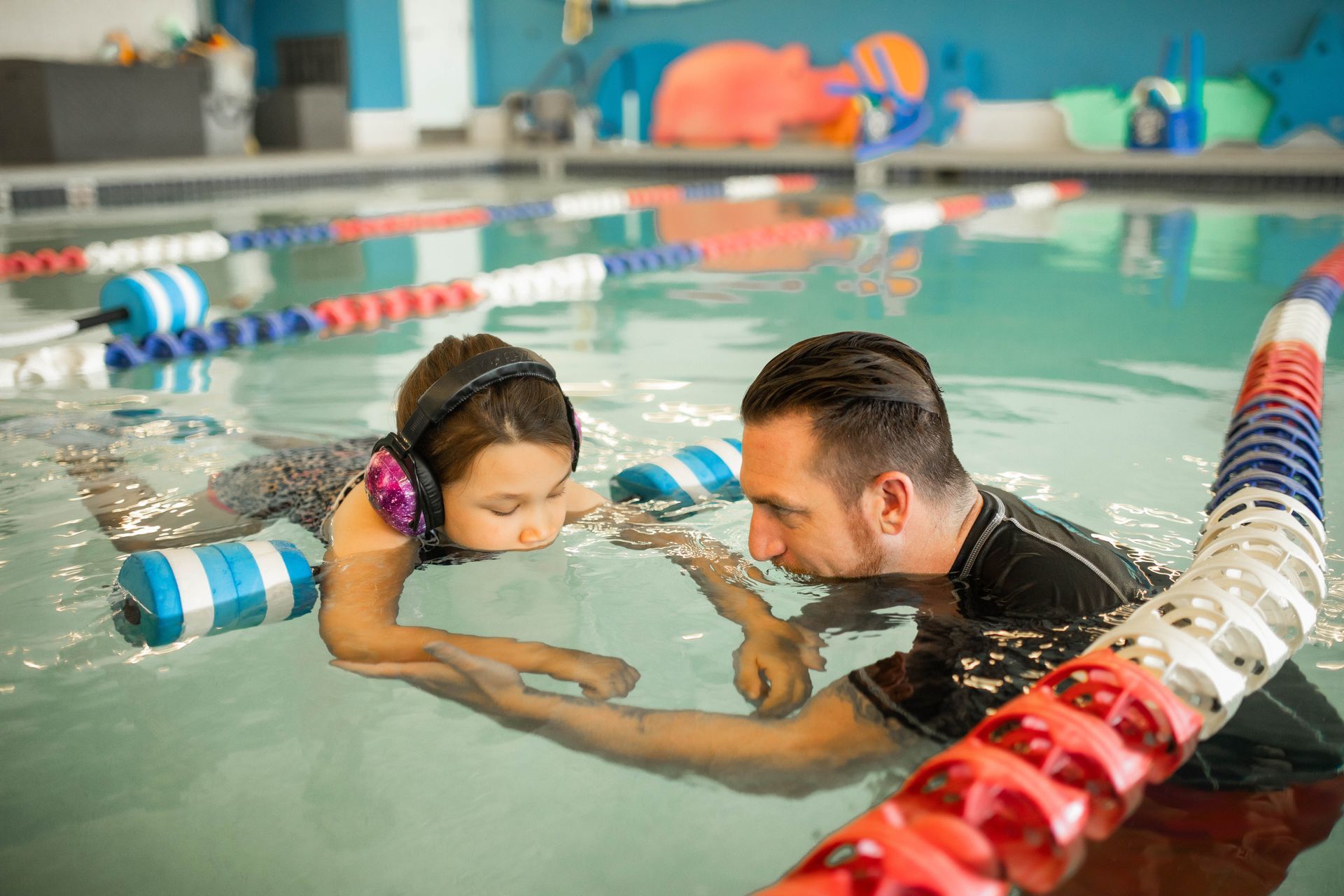 A man is teaching a little girl how to swim in a swimming pool.