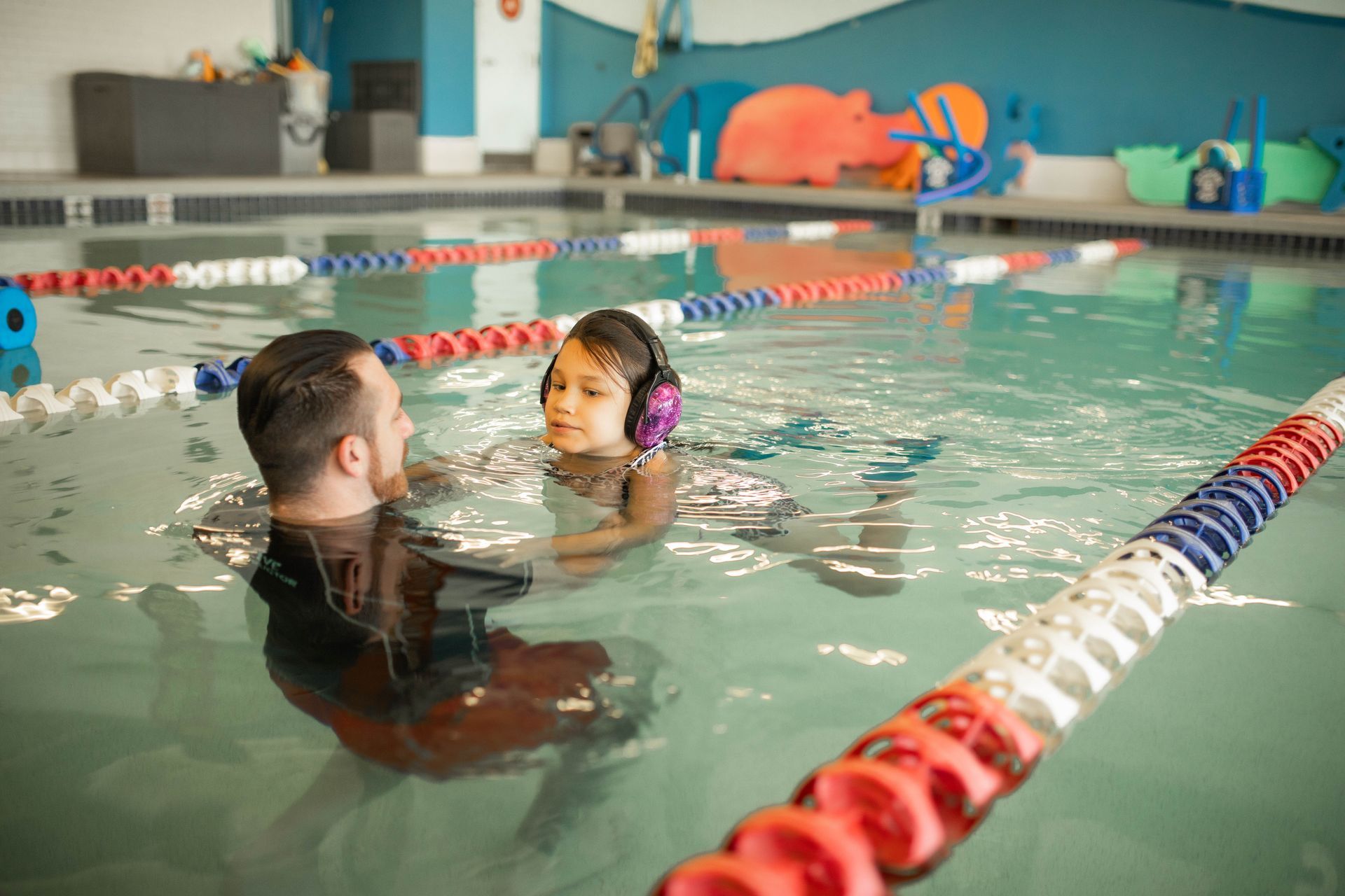 A man is teaching a little girl how to swim in a swimming pool.