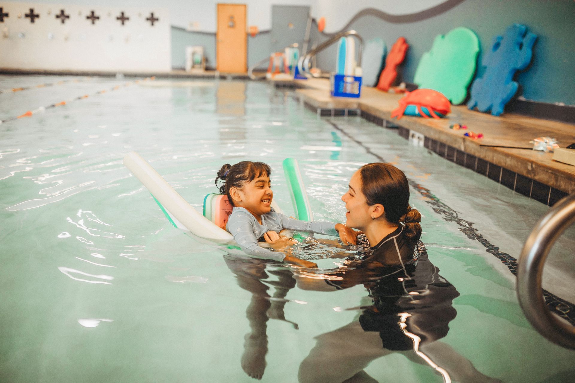 A woman is teaching a little girl how to swim in a swimming pool.