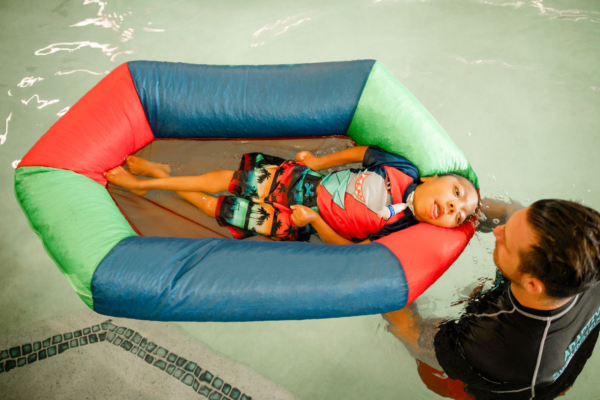 A man is holding a child in an inflatable boat in a swimming pool.