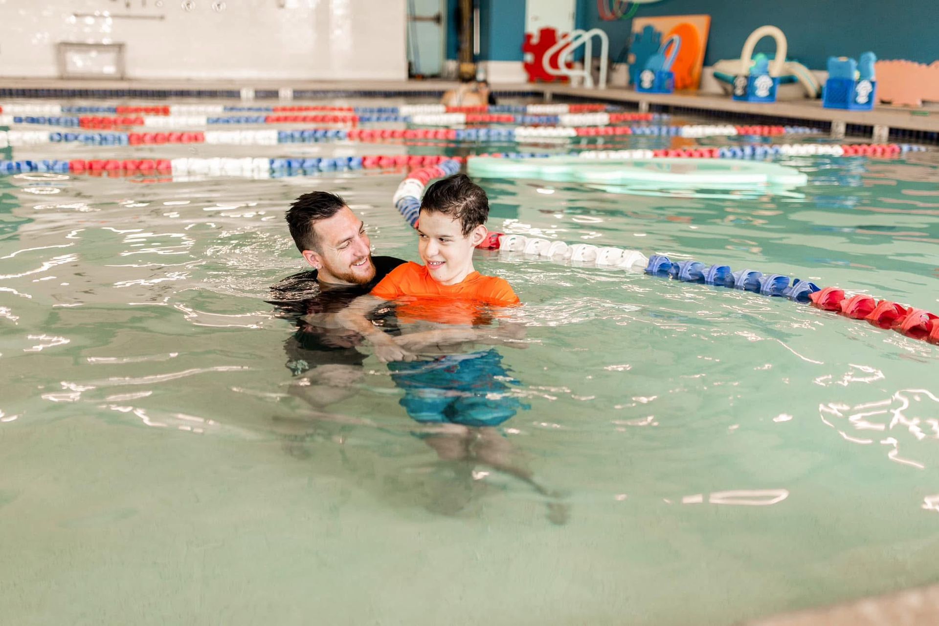 A man is teaching a young boy how to swim in a swimming pool.