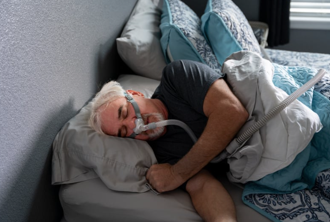 A man is sleeping in a bed with an oxygen mask on his face.