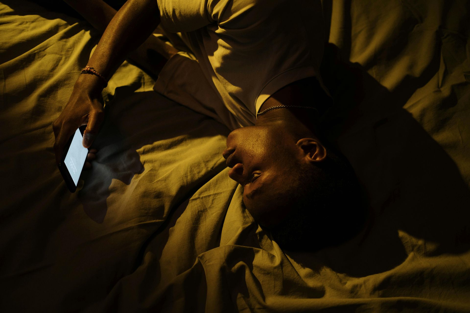 A man is laying on a bed looking at his cell phone.