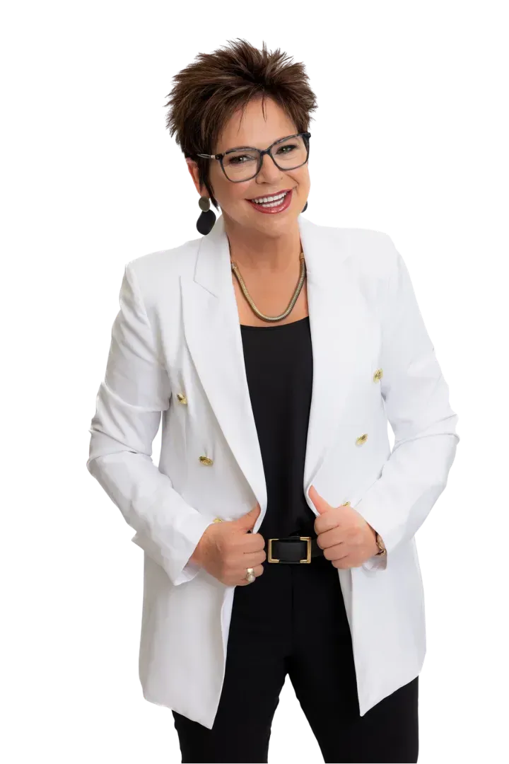 A person with short dark hair and glasses wears a white blazer over a black top, smiling while posing against a white background.
