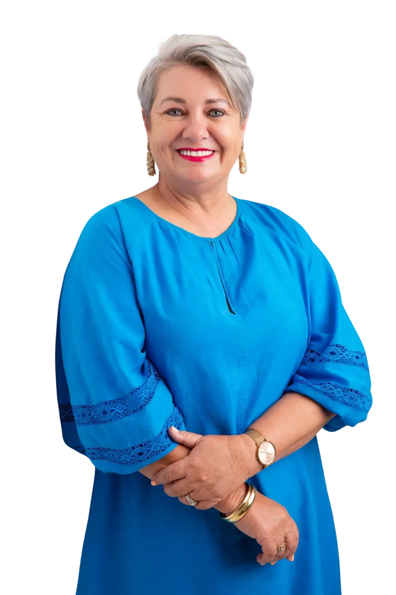 A smiling person with short gray hair, wearing a bright blue long-sleeved dress and gold jewelry, posing against a white background.