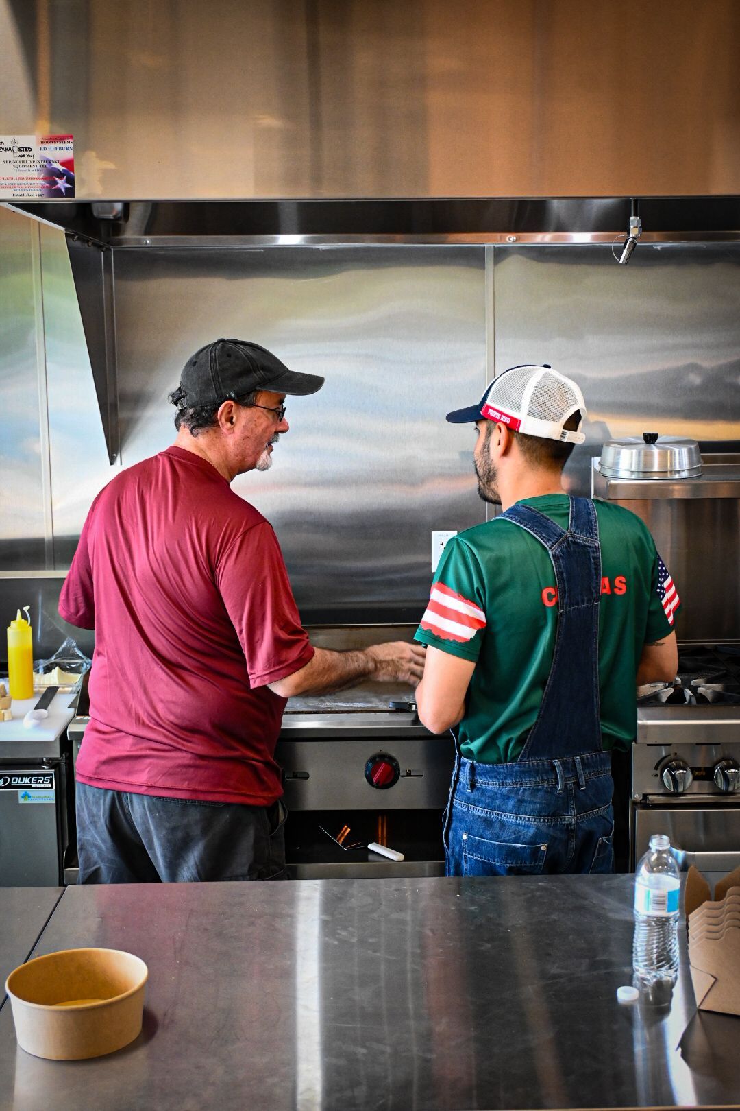 Two men are standing in a kitchen preparing food on a grill.