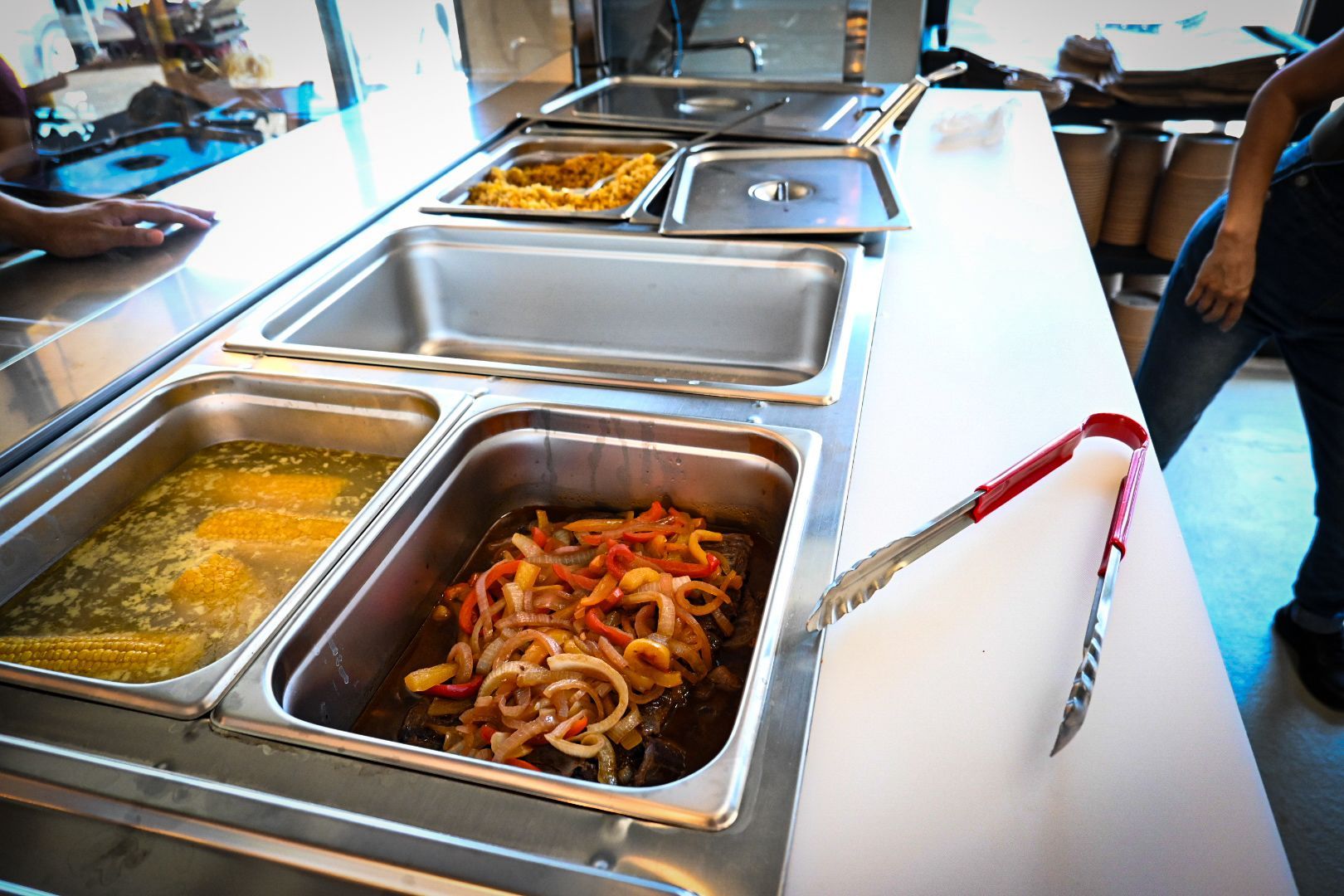 A buffet line with trays of food and tongs on a counter.