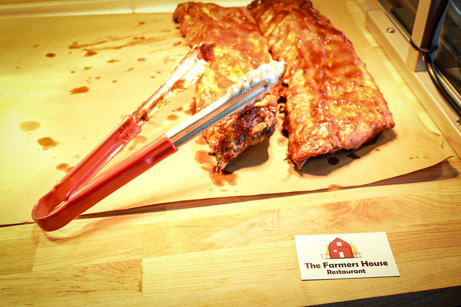 A pair of tongs holding a piece of meat next to a sign that says the farmhouse restaurant