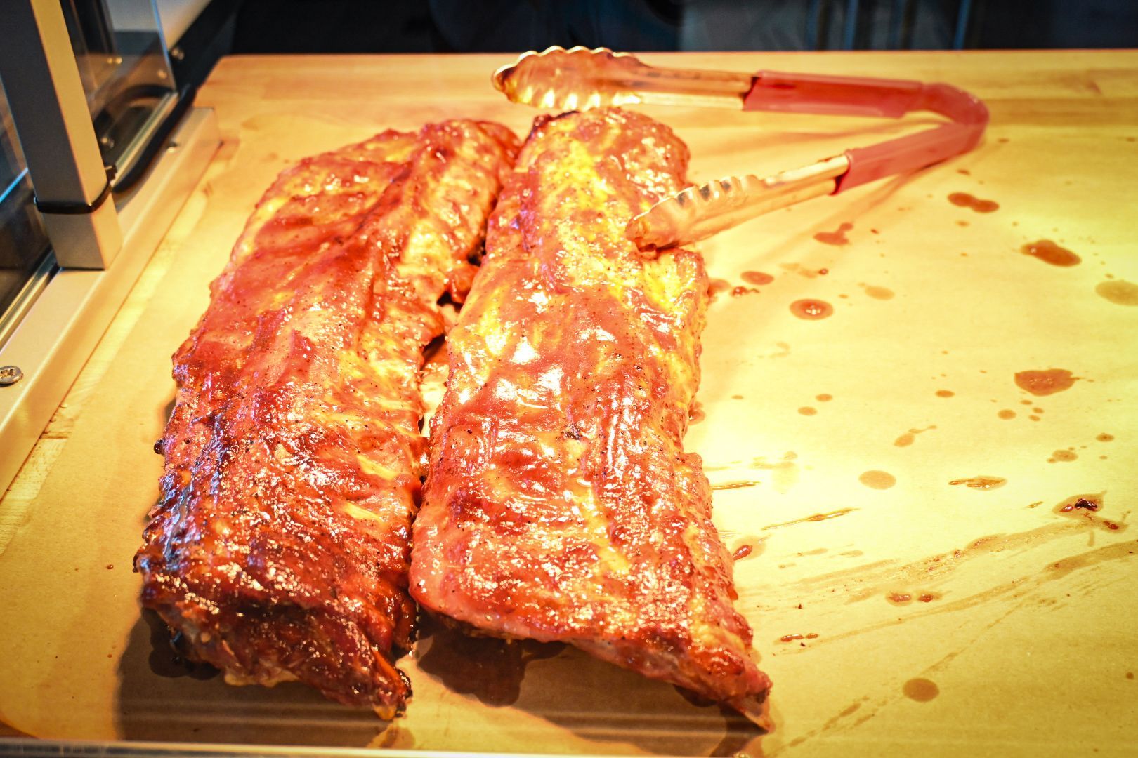 A cutting board with ribs and tongs on it