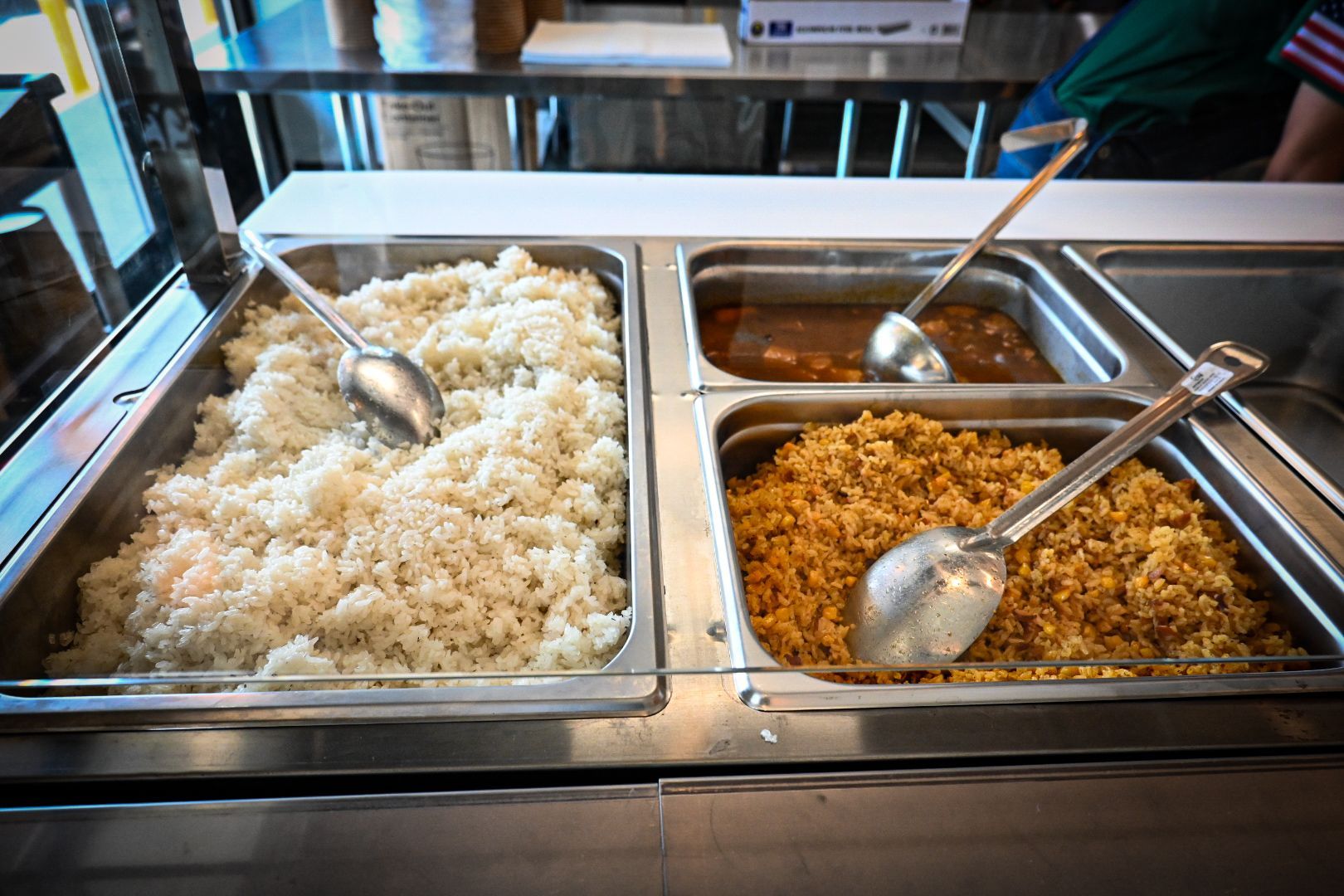Two trays of food with spoons in them are on a buffet line.