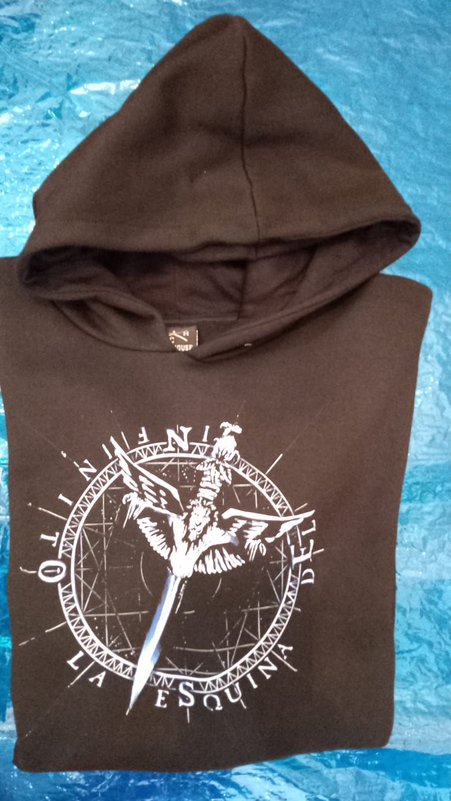 Sudadera marrón con capucha, con un gráfico circular blanco y texto sobre una superficie azul.