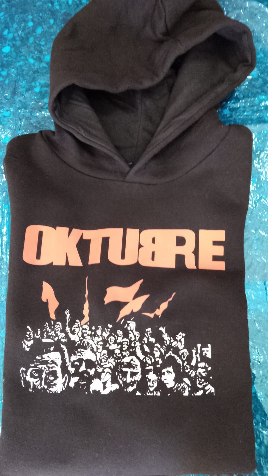 Sudadera negra con capucha, con el texto naranja “OKTU8RE” y un gráfico de una multitud blanca en el pecho.