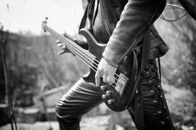 Primer plano en blanco y negro de una persona tocando el bajo eléctrico al aire libre.