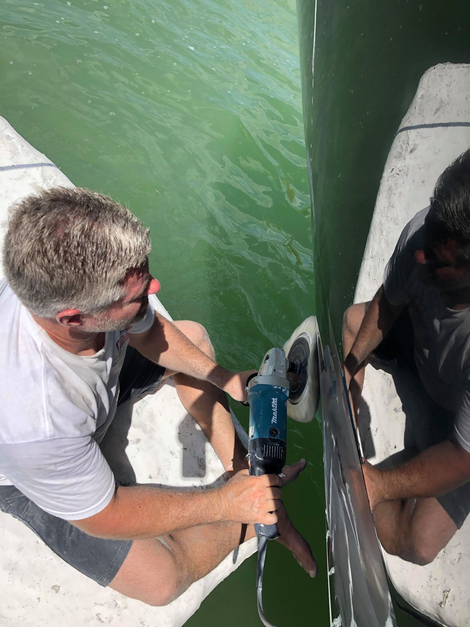 Two men are polishing a boat in the water.