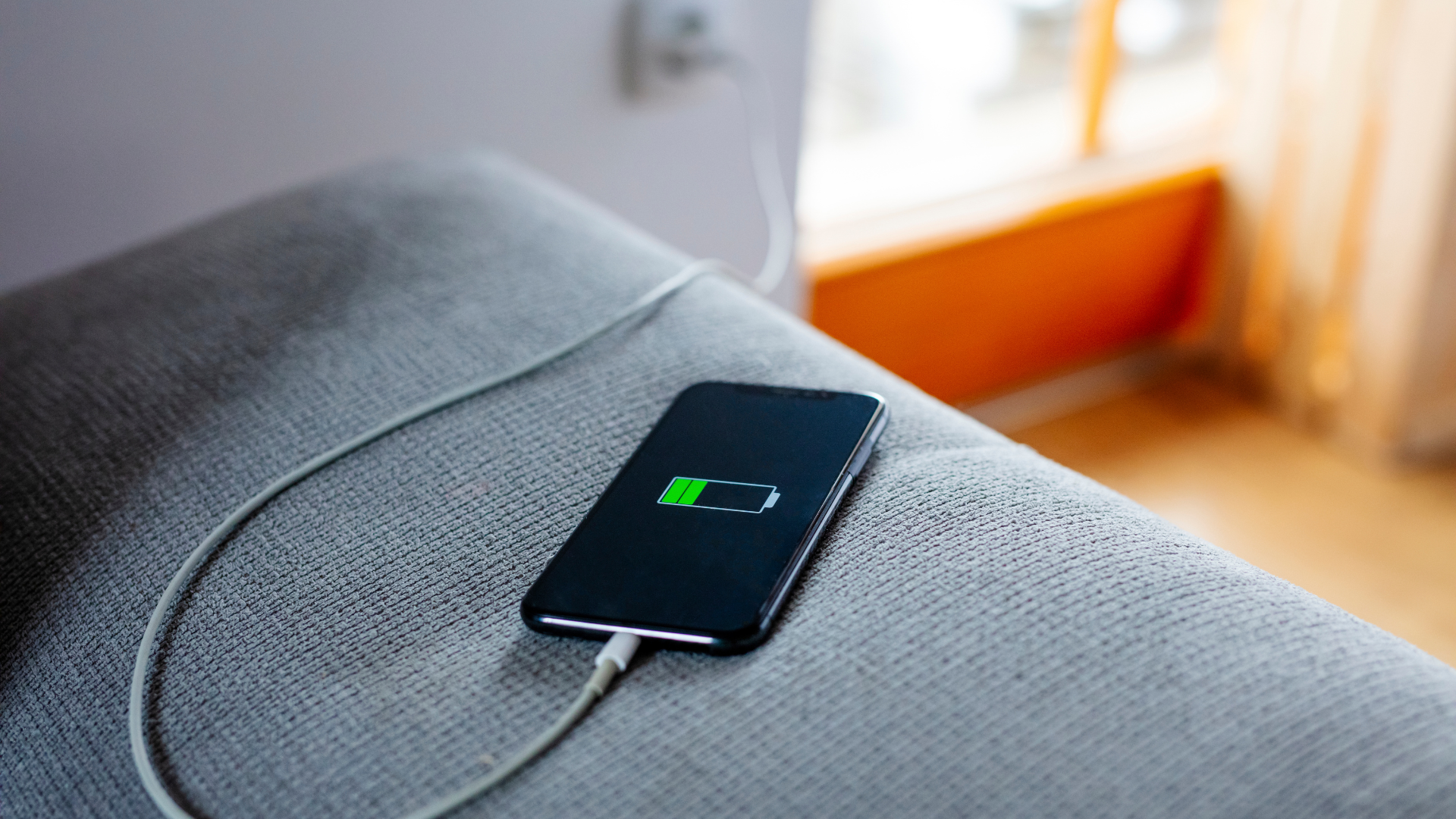 Smartphone in carica appoggiato su un divano, collegato a un caricabatterie inserito nella presa.