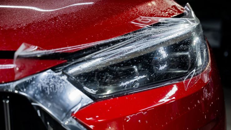 Red car headlight with protective film applied, capturing water droplets.