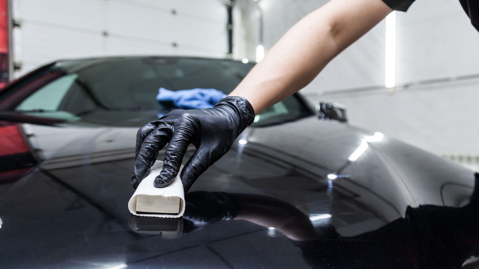 Person wearing a black glove applying sealant to a black car's hood.