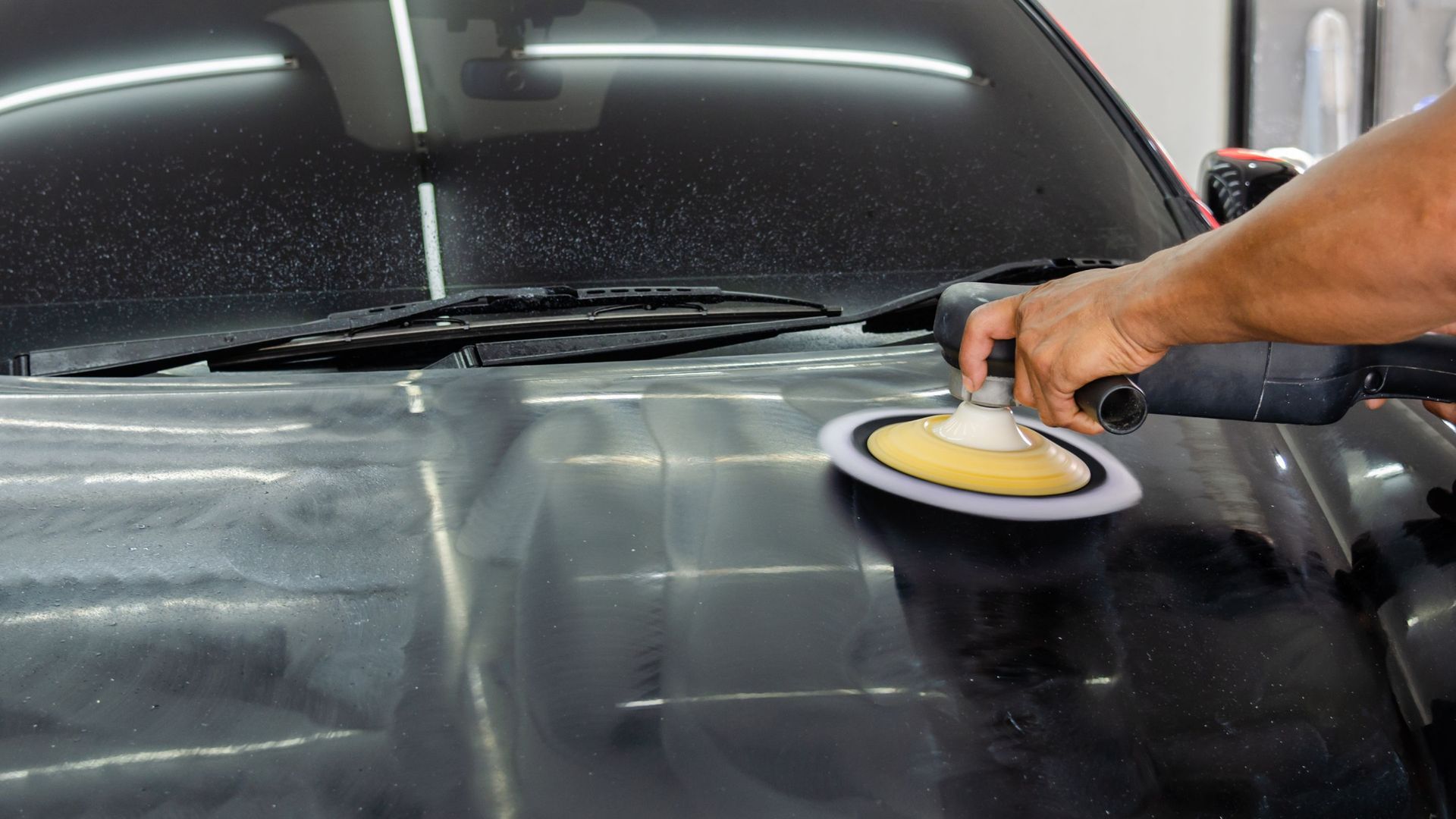 Person using a buffer on a car hood to polish it.