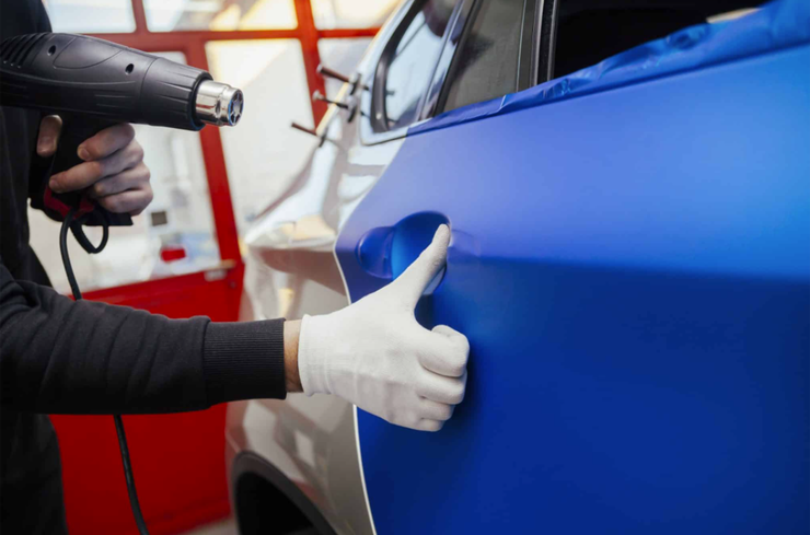 Person applying blue vinyl wrap to a car door with a heat gun.