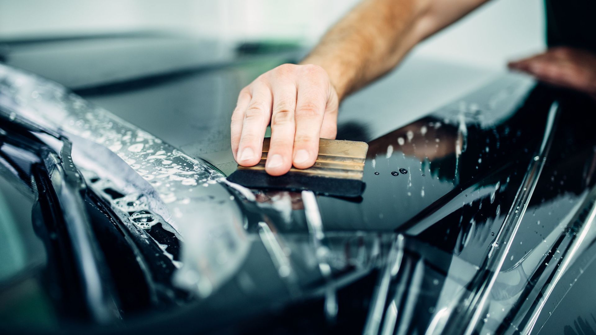 Hand applying window tint film to car windshield.