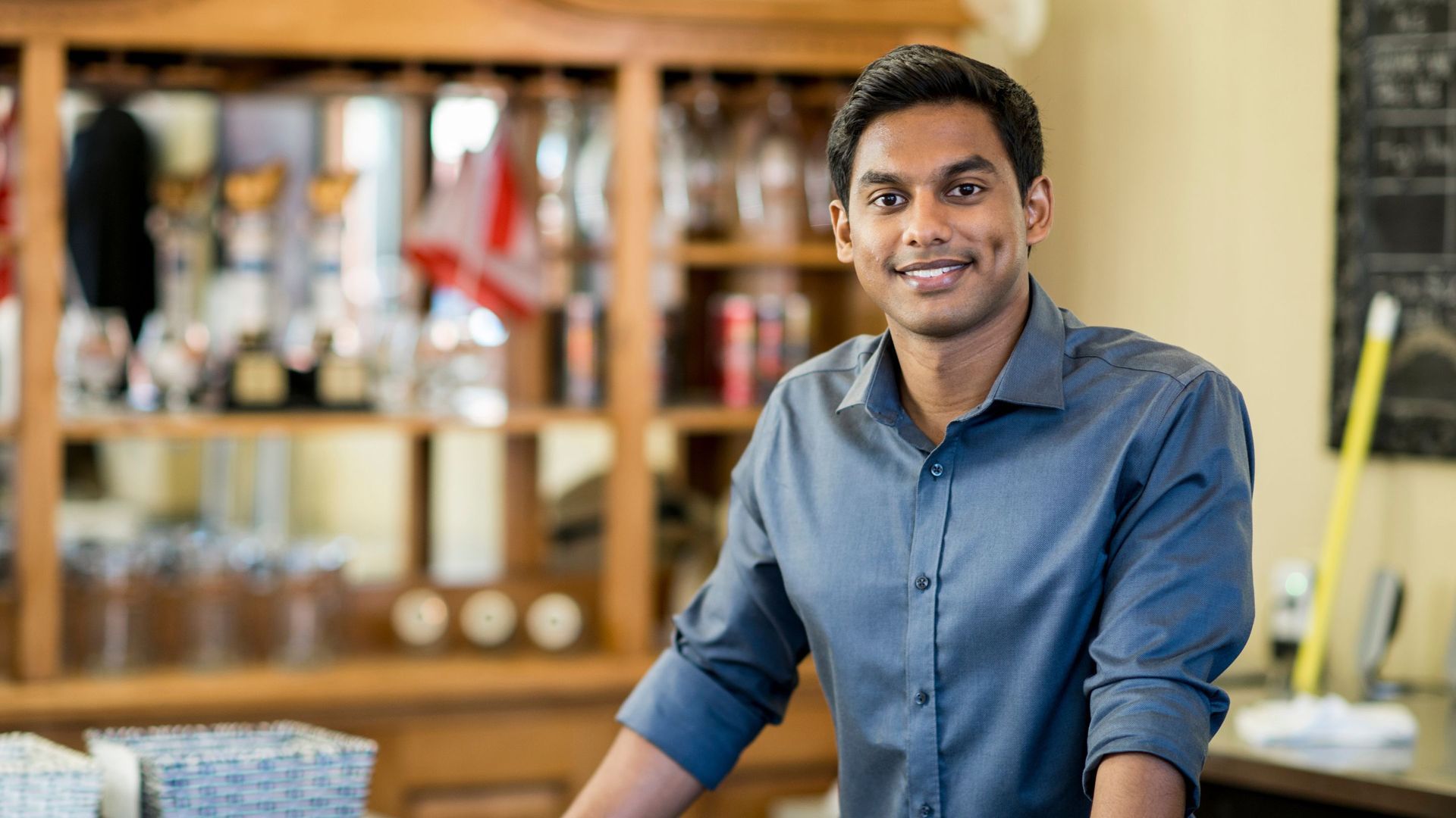 Man in blue shirt smiles behind a bar.