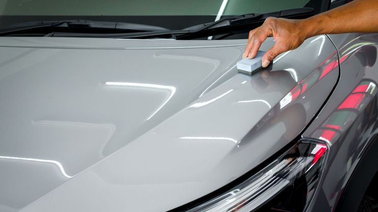 Hand applying ceramic coating to a silver car hood in a garage.
